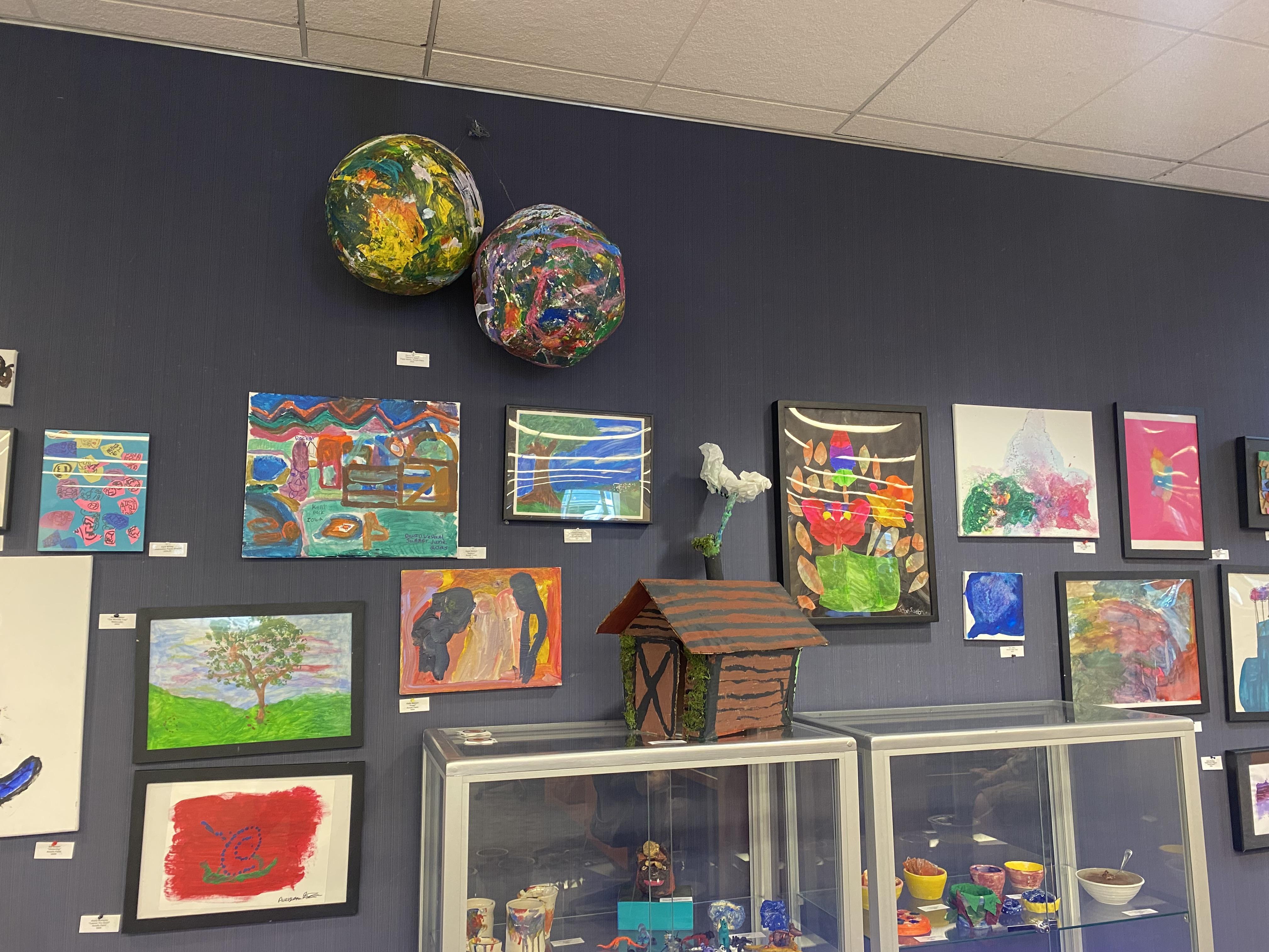 Many pieces of 2-D art, such as paintings and drawings, are hanging against the wall. Some 3-D art, such as ceramics and other sculptures, are displayed in glass cases and hanging from the ceiling. 
