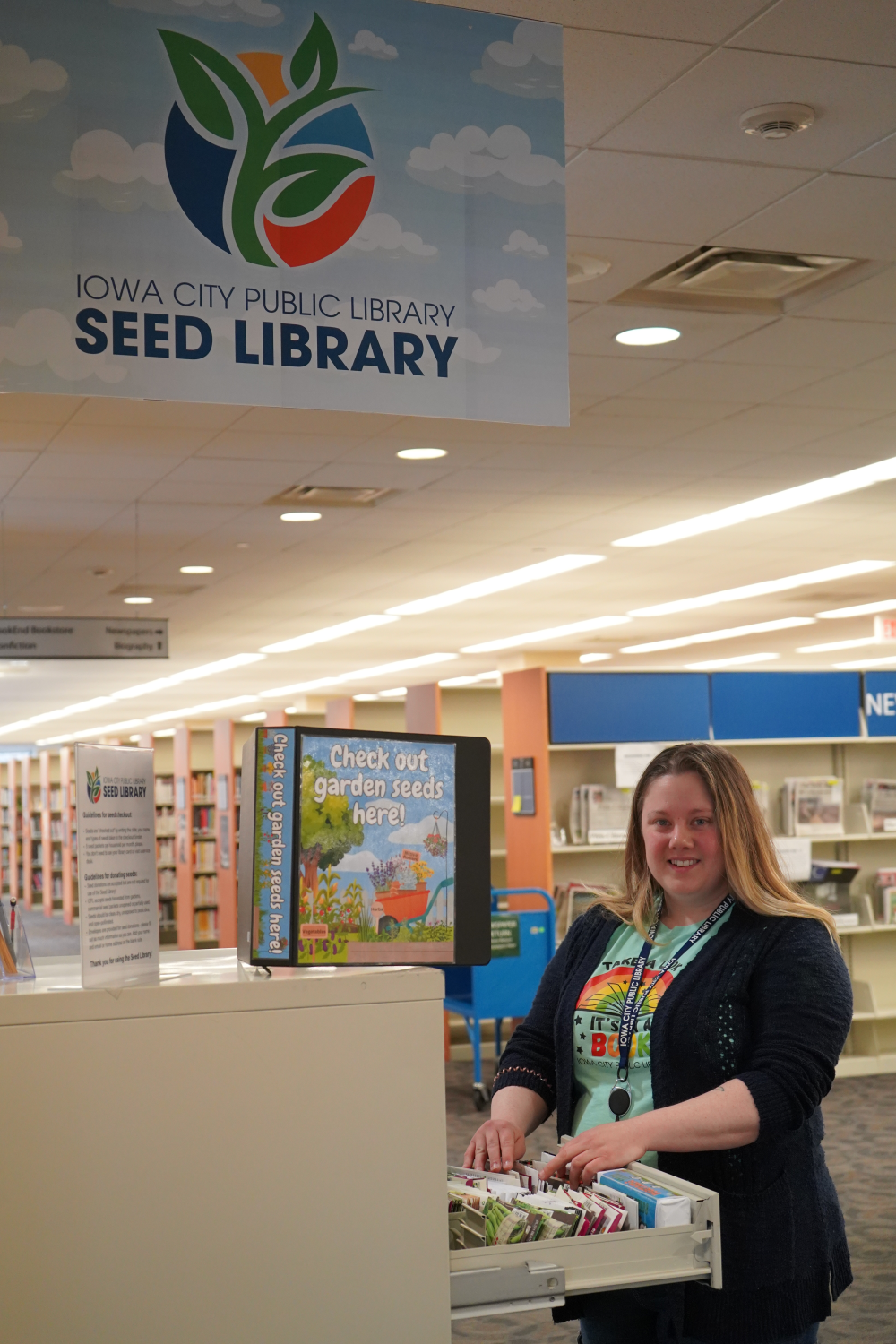 A woman on the second floor of the Iowa City Public Library looks through seed packets in the drawer of a file cabinet that has been repurposed as a Seed Library. 
