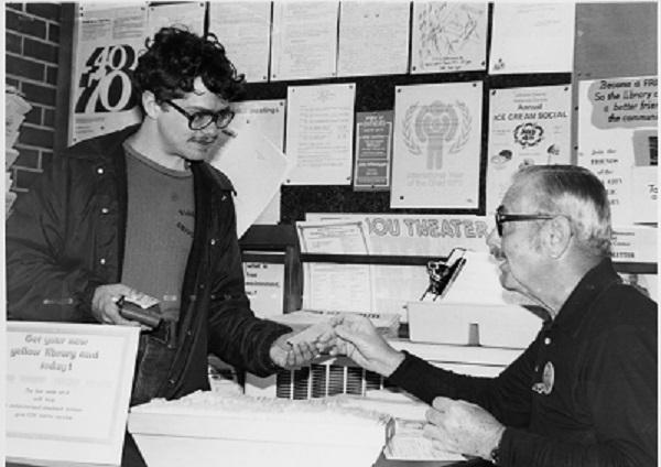 A young man hands an older man his ICPL library card at the checkout desk