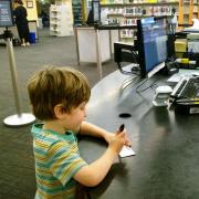 a young child writes on the back of a library card at the help desk